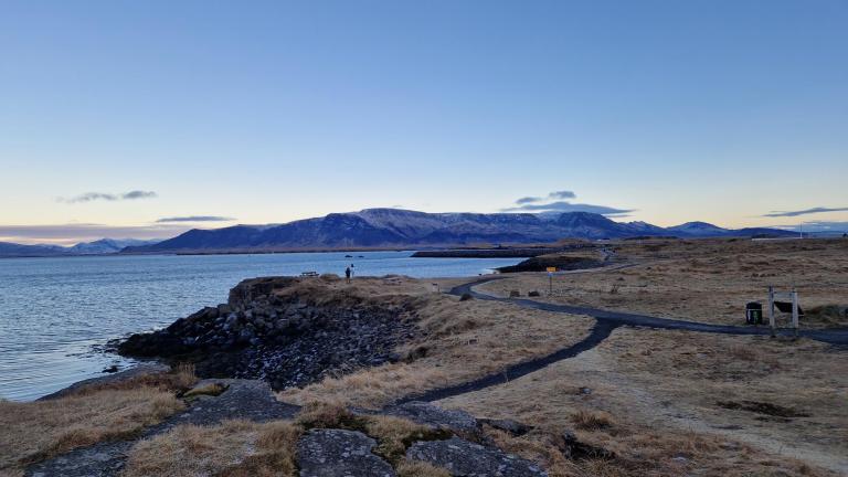 Laugarnestangi, horft yfir grösugt svæðið og göngustíg. Sjórinn og fjöllin í fjarska. Kuldalegt, heiður himinn.