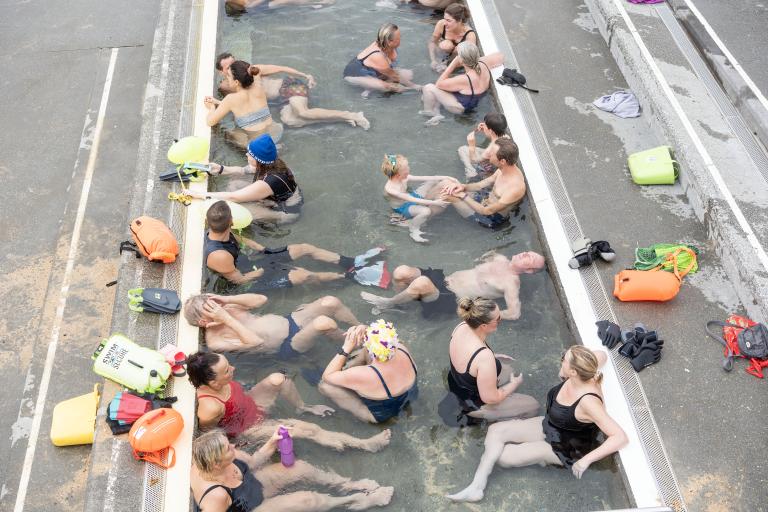 Fólk í heita pottinum á Ylströndinni í Nauthólsvík. Mynd tekin ofan frá. Búnaður til sjósundsiðkunar á bakkanum.