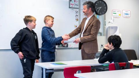 Dagur B. Eggertsson borgarstjóri veitir viðtöku undirskriftalista frá börnum í Landakotsskóla. Á myndinni tekur hann í hönd annars drengjanna sem stóðu að listanum, hinn fylgist með ásamt einu barni enn, sem situr. Mynd úr skólastofu.