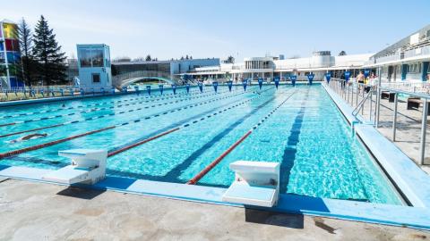 Horft yfir 50 metra laug Laugardalslaugar úti, frá dýpri endanum. Blár himinn.