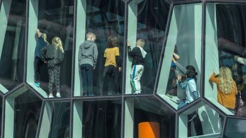 Mynd tekin inn um glugga á Hörpu, sést aftan á nokkur börn sem standa í gluggunum.