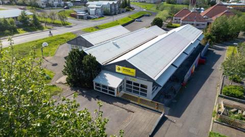 Séð ofanfrá á aflangt hús sem hýsir félagsmiðstöðina Hólmasel. Græn lauf í forgrunni. 