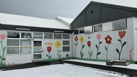 Hvítt hús með máluðum blómum á, sem hýsir frístundaheimilið Regnbogann. 