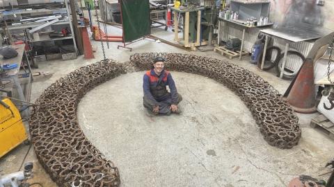 Vinnustofa, maður situr á gólfi, listaverk úr skeifum í kring.