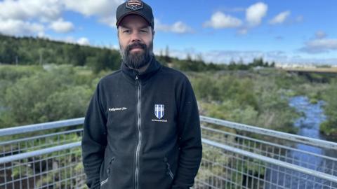 Man on a bridge with forest and river in the background.