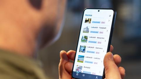 maður að nota appið Bara tala. Óljós vangasvipur mannsins, hönd hans og sími í hönd, með appið opið
