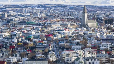 Aerial view of Reykjavík in winter. Snow, white mountains in the background, Hallgrímskirkja on the right side of the frame in the center, Tjörnin in the foreground.