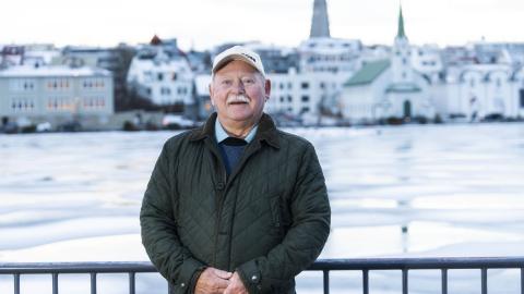 Portrait of Einar D. G. Gunnlaugsson. Standing on the viewing platform by the Tjörnin pond with the pond, Fríkirkja, and Hallgrímskirkja in the background. Winter, ice.