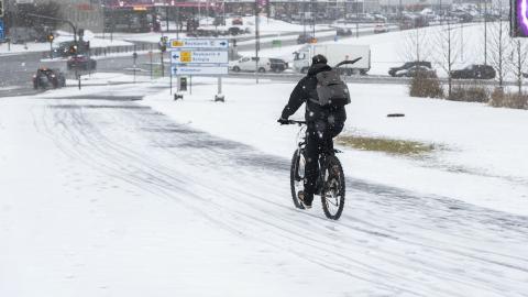 A cyclist on a snow-covered road with buildings nearby.