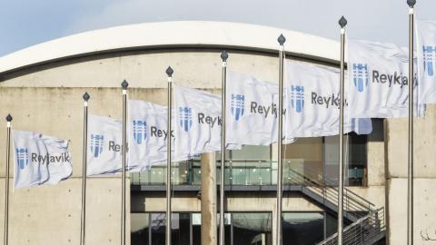 Ráðhús Reykjavíkur, fánaborg á brúnni í forgrunni, nærmynd af fánum borgarinnar og sést í húsið í bakgrunni