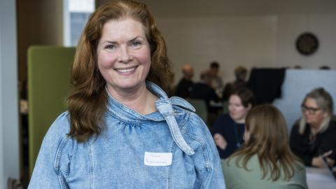 Kona að brossa með fólk í baksýn.