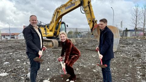 Two men and one woman break ground with an excavator in the background