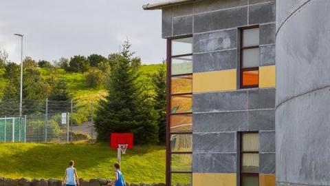 Mynd af húsaskóla. Tvö börn spila körfubolta á leikvelli.