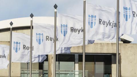 Nærmynd af Reykjavíkurfánum á brúnni við Tjörnina, fánarnir sjálfir og sést í Ráðhúsið í bakgrunni.