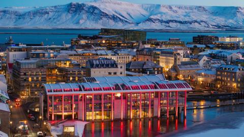 Ráðhúsið lýst rautt í forgrunni, í bakgrunni Miðborgin og Esjan. Skuggsýnt, desember.