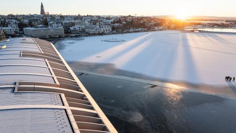Þak Ráðhússins í forgrunni, ísilögð Tjörn, sólin að koma upp í fjarska. Hallgrímskirkja og Þingholtin í bakgrunni.
