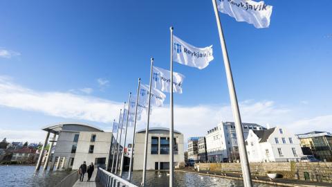 Ráðhús Reykjavíkur, horft frá enda brúarinnar. Reykjavíkurfána flaggað á fánaröð brúar. Blár himinn.
