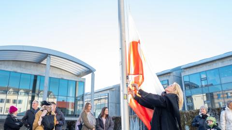 Mayor Heiða Björg Hilmisdóttir raises the Greenlandic flag at full staff at Reykjavík City Hall. City Hall and onlookers in the background.