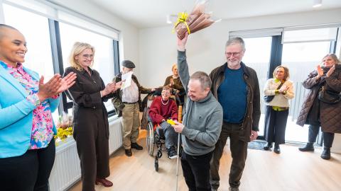 Kjartan Ásmundsson lyftir blómum upp í loft eins og bikar til að fagna því að hafa fengið lykla að íbúð sinni. Á myndinni eru líka borgarstjóri og formaður velferðarráðs. 