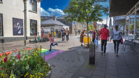 Fólk á gangi, blóm og tré.