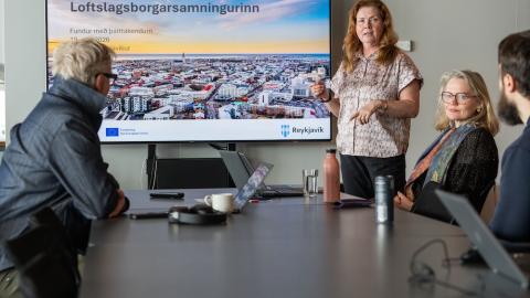 Fólk við borð og skjár í baksýn