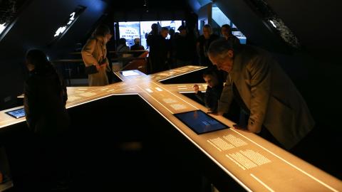 Visitors at the Settlement Exhibition on Aðalstræti. A dimly lit space with people gathered around an illuminated scale model of streets.